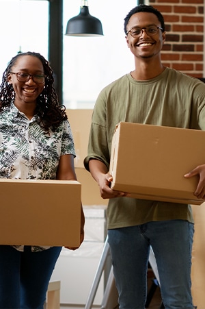 Close up of young spectacled Afro Caribbean man and woman holding brown packing boxes