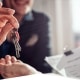 Close up of keys on a key ring being handed over from a woman in business dress to a man's hand holding bull clipped paperwork in the other hand