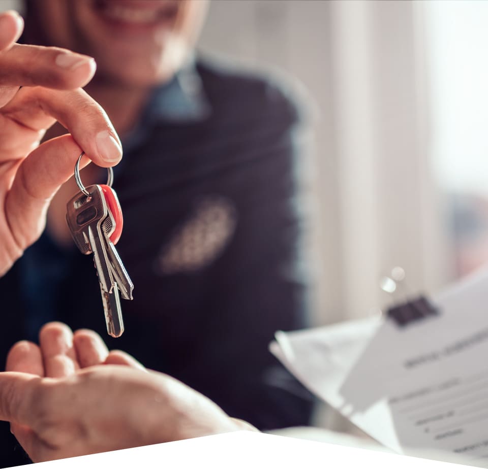 Close up of keys on a key ring being handed over from a woman in business dress to a man's hand holding bull clipped paperwork in the other hand