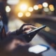 Evening image of woman touching backlit mobile phone screen with dappled street lights in the background