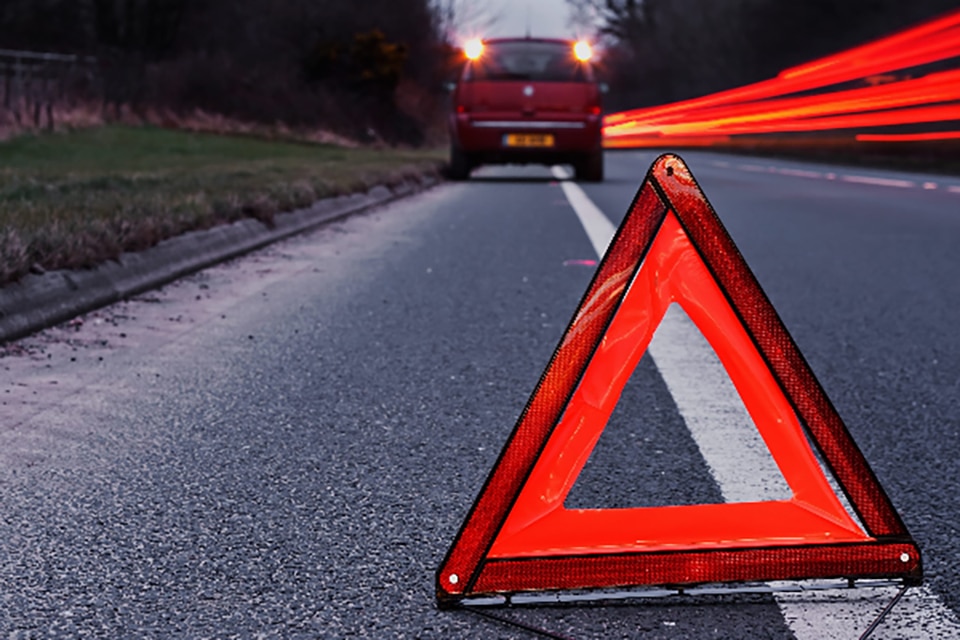 Evening image of car parked at the roadside with red hazard triangle in the foreground