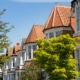 Close up traditional row of bay fronted sash window terraced properties with lush green trees and blue sky