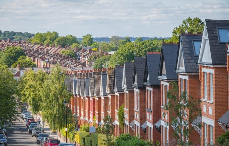 Hillside row of red brick terraced houses tree lined street with parked cars leading down to more rows of terraced rooftops and chimney tops