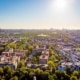 Pan aerial view of a large town with far reaching views blocks of traditional red brick apartment blocks and houses in the foreground with tree lined streets and a large park with lake in the middle distance and tall city building skyline