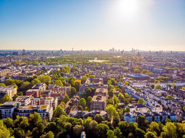 Pan aerial view of a large town with far reaching views blocks of traditional red brick apartment blocks and houses in the foreground with tree lined streets and a large park with lake in the middle distance and tall city building skyline