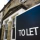 Dark blue To Let sign with white text outside entrance to a period property with stone mullion windows and ornate stone brick work