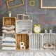 Display of wooden crates some painted white filled with cushions trainers books candles lamps cactus plants letter B frames graphics on wall and stripe textured neutral rug on floor