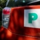 Rear of red orange car with green and white provisional new driver P sticker on boot tailgate next to rear lights