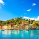 Multi coloured lakeside Italian houses in Portofino wrapped around wooded headland with small boats moored in front