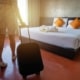 King size hotel bedroom with towels and pamper tray on white bedding with woman in summer dress and trainers with small suitcase on wheels