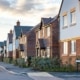 Row of new build detached houses some brick some rendered some with canopied front doors and others with bay windows and hedging to front gardens