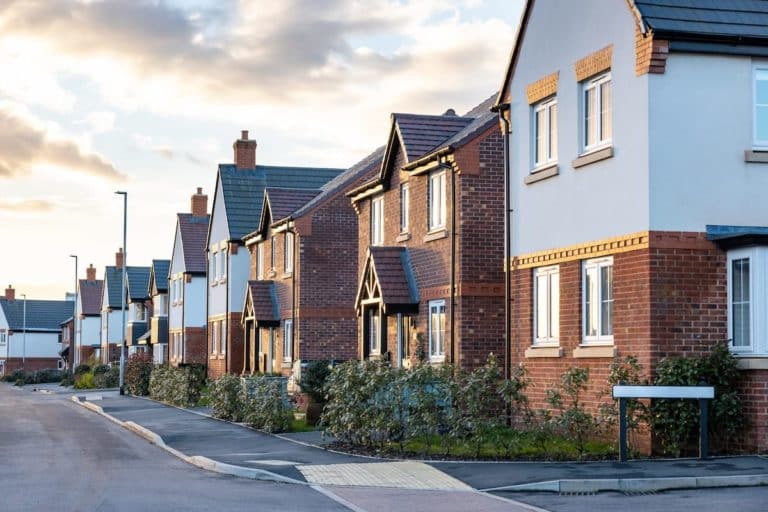 Row of new build detached houses some brick some rendered some with canopied front doors and others with bay windows and hedging to front gardens