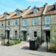 Row of new build stone fronted three storey homes with ornate metal railings and attic roof windows