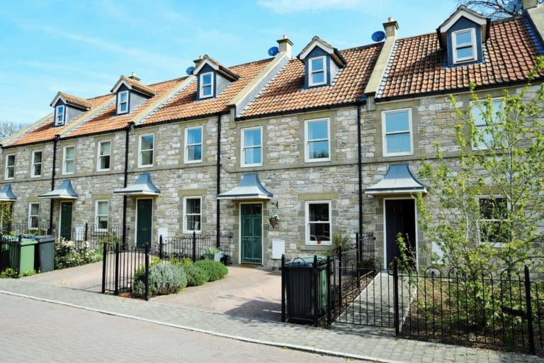 Row of new build stone fronted three storey homes with ornate metal railings and attic roof windows